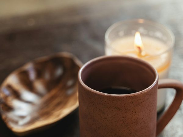 Tasse Kaffee neben brennender Kerze auf einem Tisch