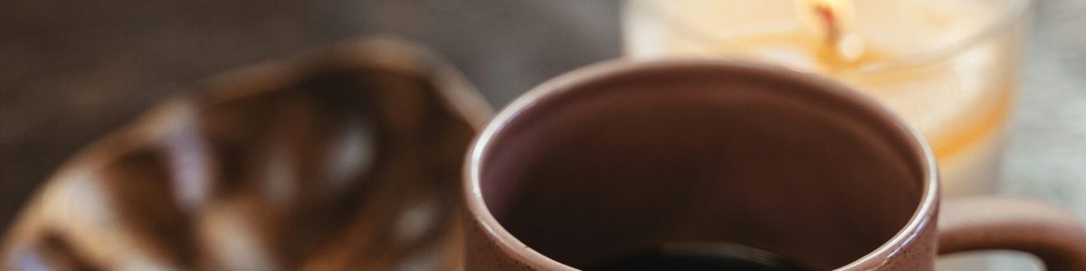 Tasse Kaffee neben brennender Kerze auf einem Tisch